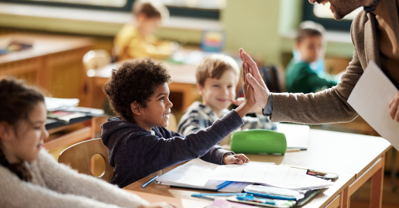 A teacher giving a student sitting at their desk a high five